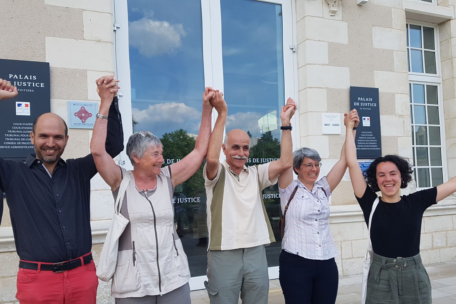 5 activistes lèvent les bras et sourient devant le palais de justice de Poitiers après leur relaxe dans leur procès pour décrochage de portrait